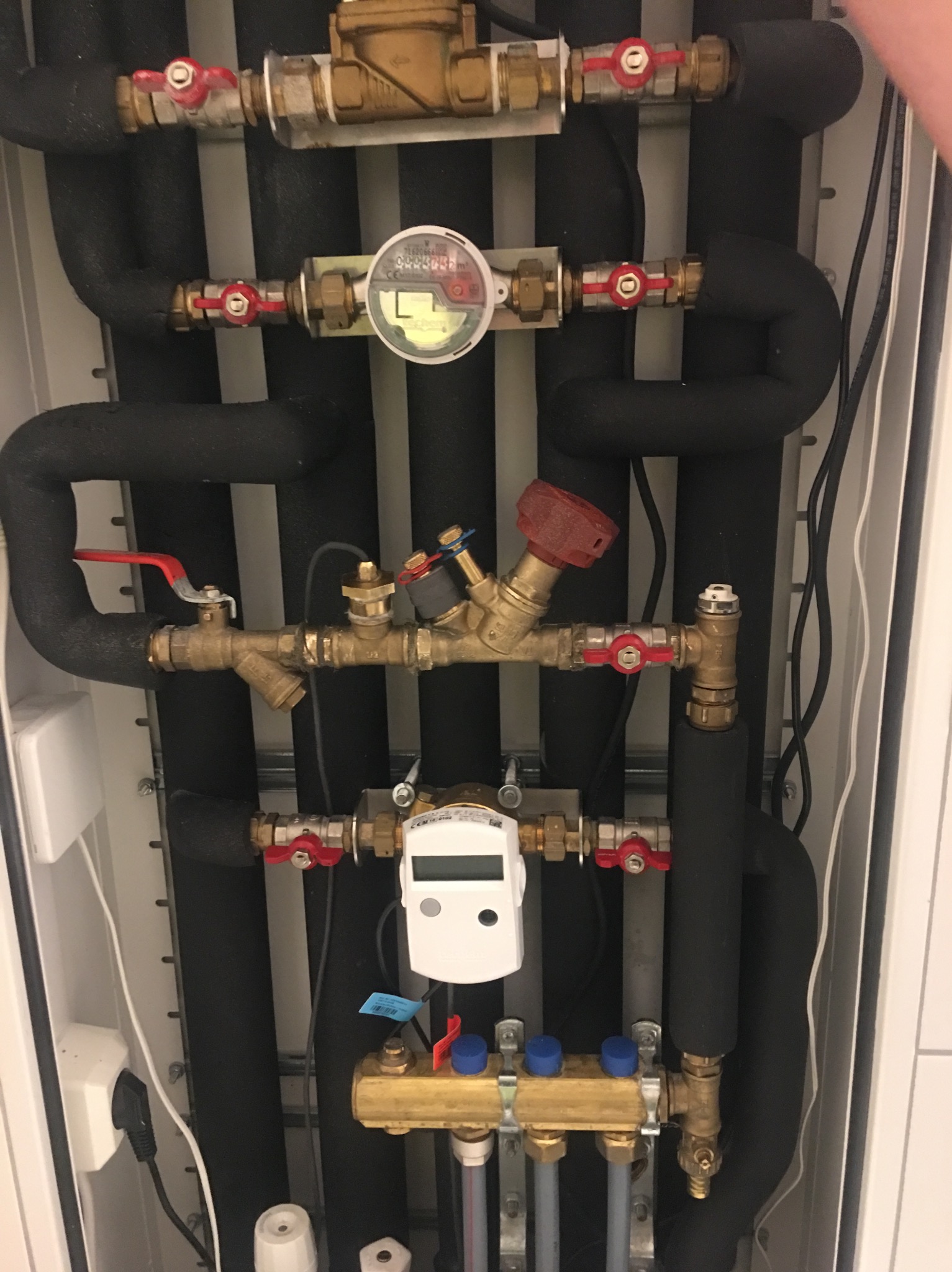 Rozdzielacz ogrzewania podłogowego z rurami w izolacji, zaworami i licznikiem ciepła w szafce instalacyjnej.