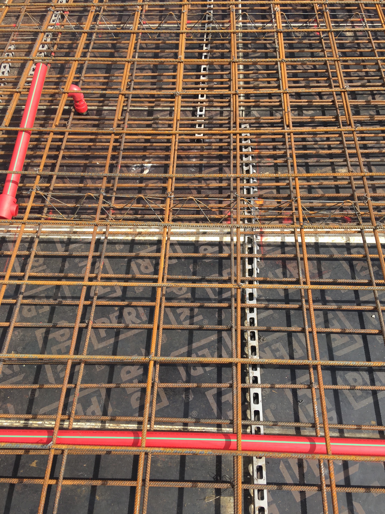 Siatka zbrojeniowa z rurami instalacyjnymi w kolorze czerwonym, przygotowana do zalania betonem.