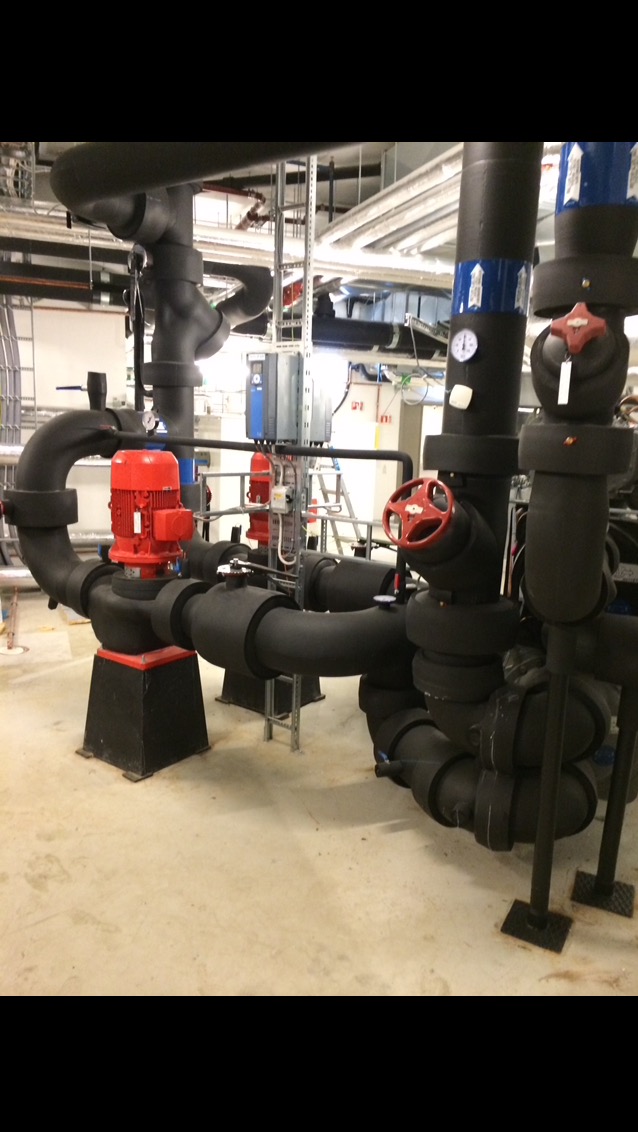 Kompleksowy system rur grzewczych z czerwonym silnikiem pompy i zaworami w Szczecinie, zaizolowane termicznie, w pomieszczeniu technicznym.