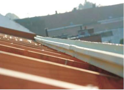 Montaż rynny dachowej z tworzywa sztucznego na drewnianej konstrukcji dachu w trakcie słonecznego dnia.