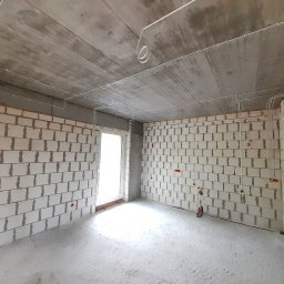 SPEC Grzegorz Piwowarski - Surowy pokój z białych bloczków, widoczne kable i puszki elektryczne na ścianach i suficie. Stan surowy, przygotowanie do dalszych prac wykończeniowych.