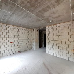 SPEC Grzegorz Piwowarski - Surowy stan wnętrza z instalacją elektryczną: przewody na suficie, puszki w ścianach z betonu komórkowego. Widok na puste pomieszczenie w trakcie prac instalacyjnych.