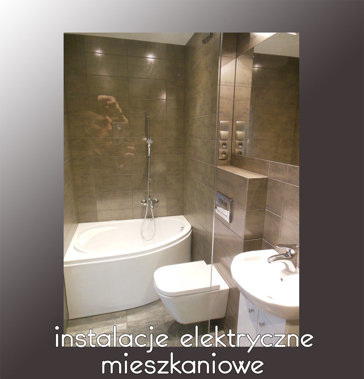 Wykończona łazienka z brązowymi płytkami, białą wanną narożną, podwieszaną toaletą i umywalką na szafce, widoczne gniazdka i włączniki elektryczne obok lustra.