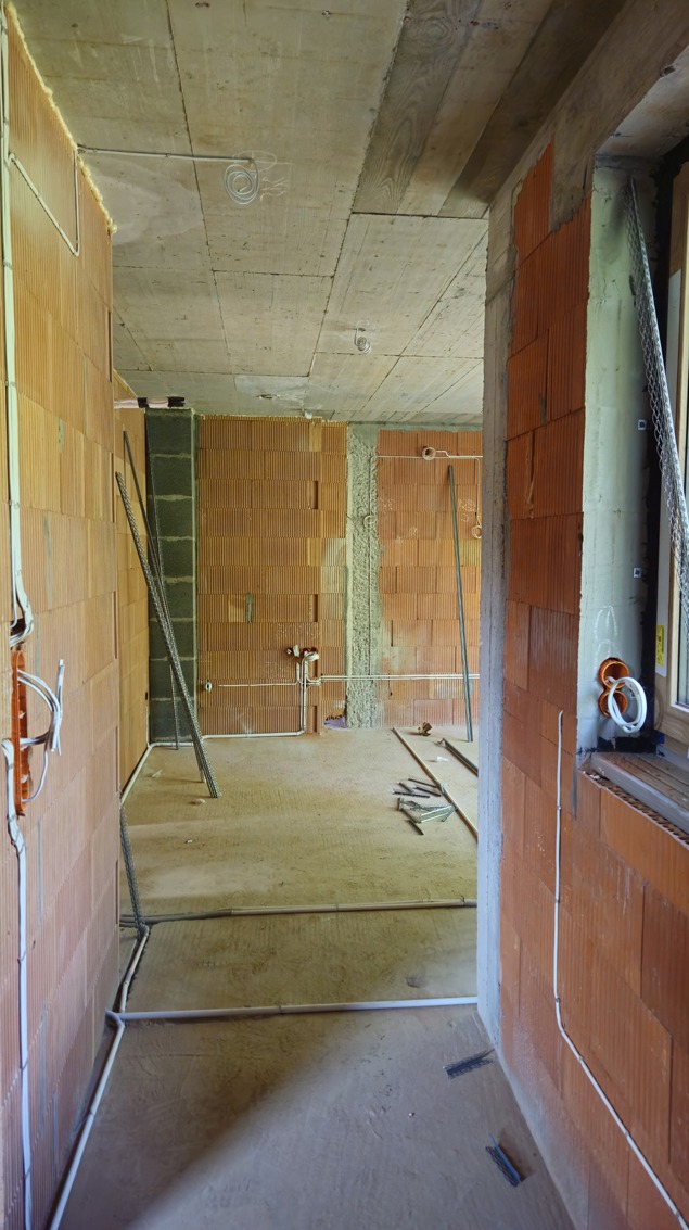 Surowy stan wnętrza z ceglanymi ścianami i widocznymi przewodami elektrycznymi, przygotowanego do dalszych prac wykończeniowych.