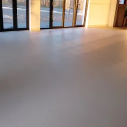 Jasna, równa wykładzina podłogowa w przestronnym pomieszczeniu z dużymi oknami tarasowymi i sprzętem do klejenia wykładzin w rogu