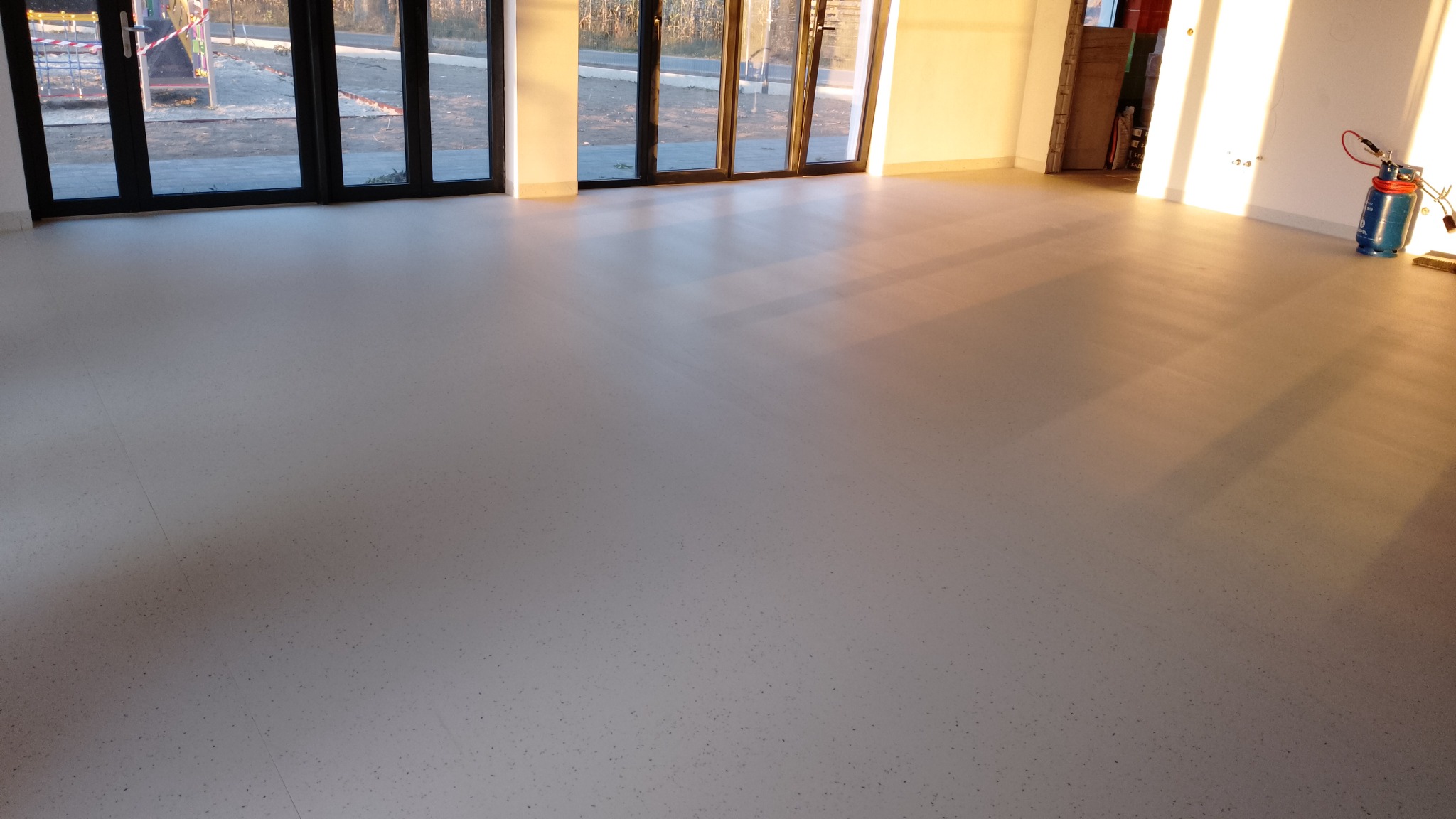 Jasna, równa wykładzina podłogowa w przestronnym pomieszczeniu z dużymi oknami tarasowymi i sprzętem do klejenia wykładzin w rogu