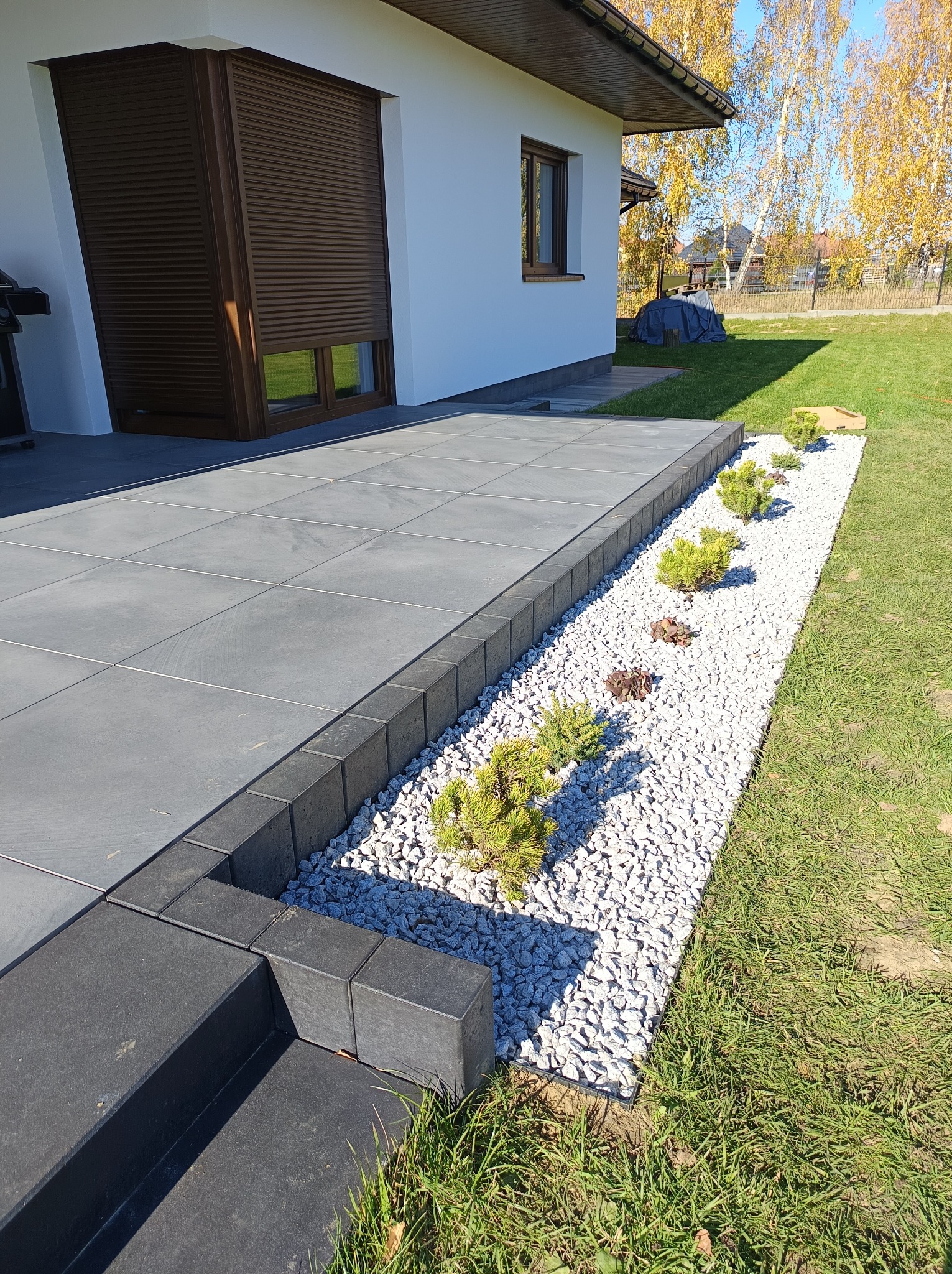 Nowoczesny ogród w Rzeszowie: Szara kostka brukowa, białe kamienie, niskie krzewy iglaste. Minimalistyczny design ogrodu przydomowego w słoneczny dzień.