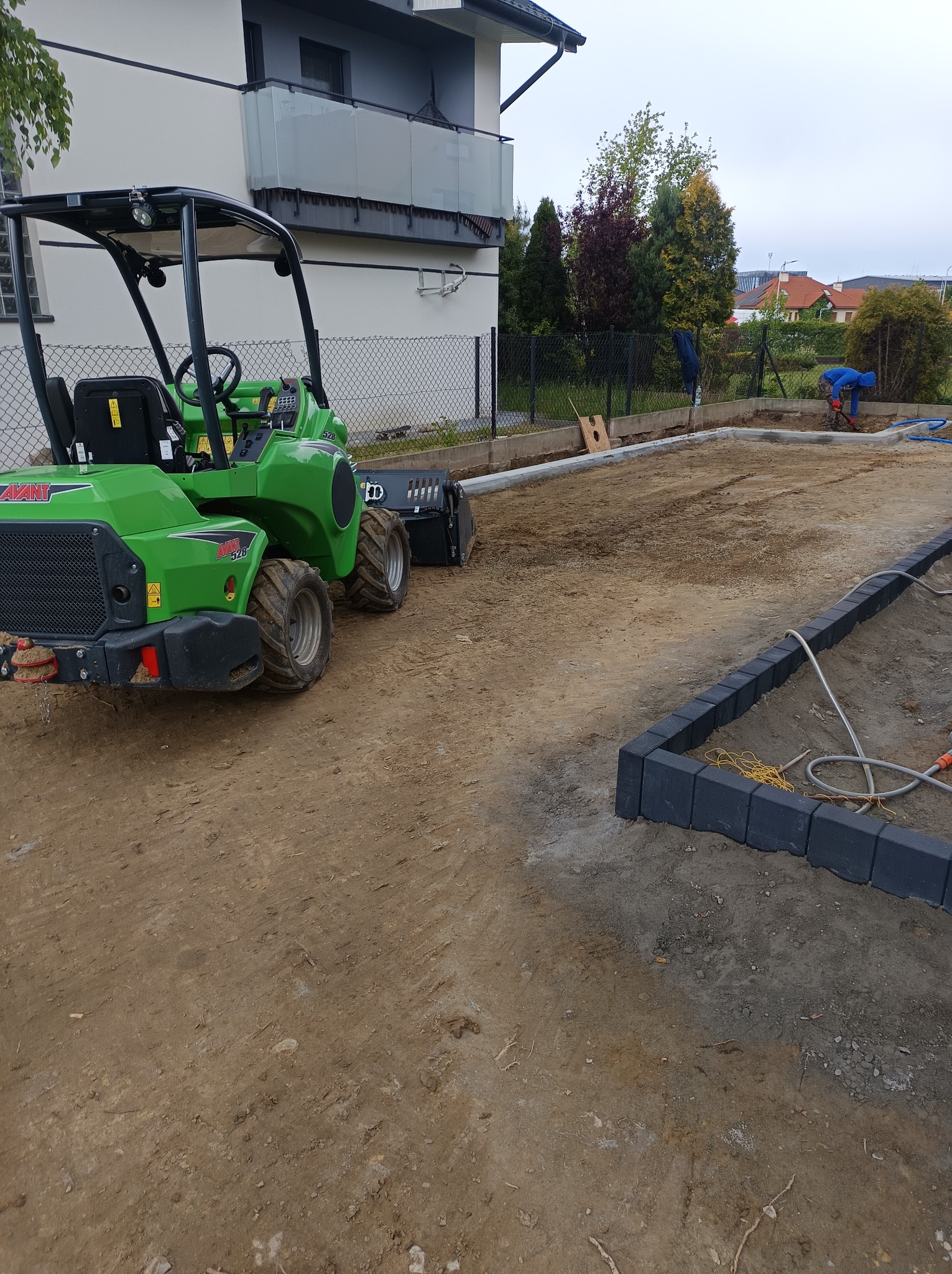 Przygotowanie terenu pod ogród z użyciem miniładowarki Avant 528. Widoczne obrzeża i pracownik w oddali.