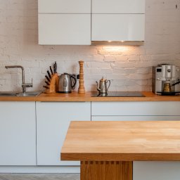 Arser Wood Polska s.c. Sławomir Brzózka, Tomasz Matosz - Nowoczesna kuchnia z białymi szafkami, drewnianym blatem i wyspą z widocznymi połączeniami stolarskimi, na tle ściany z białej cegły i parkietu w jodełkę.