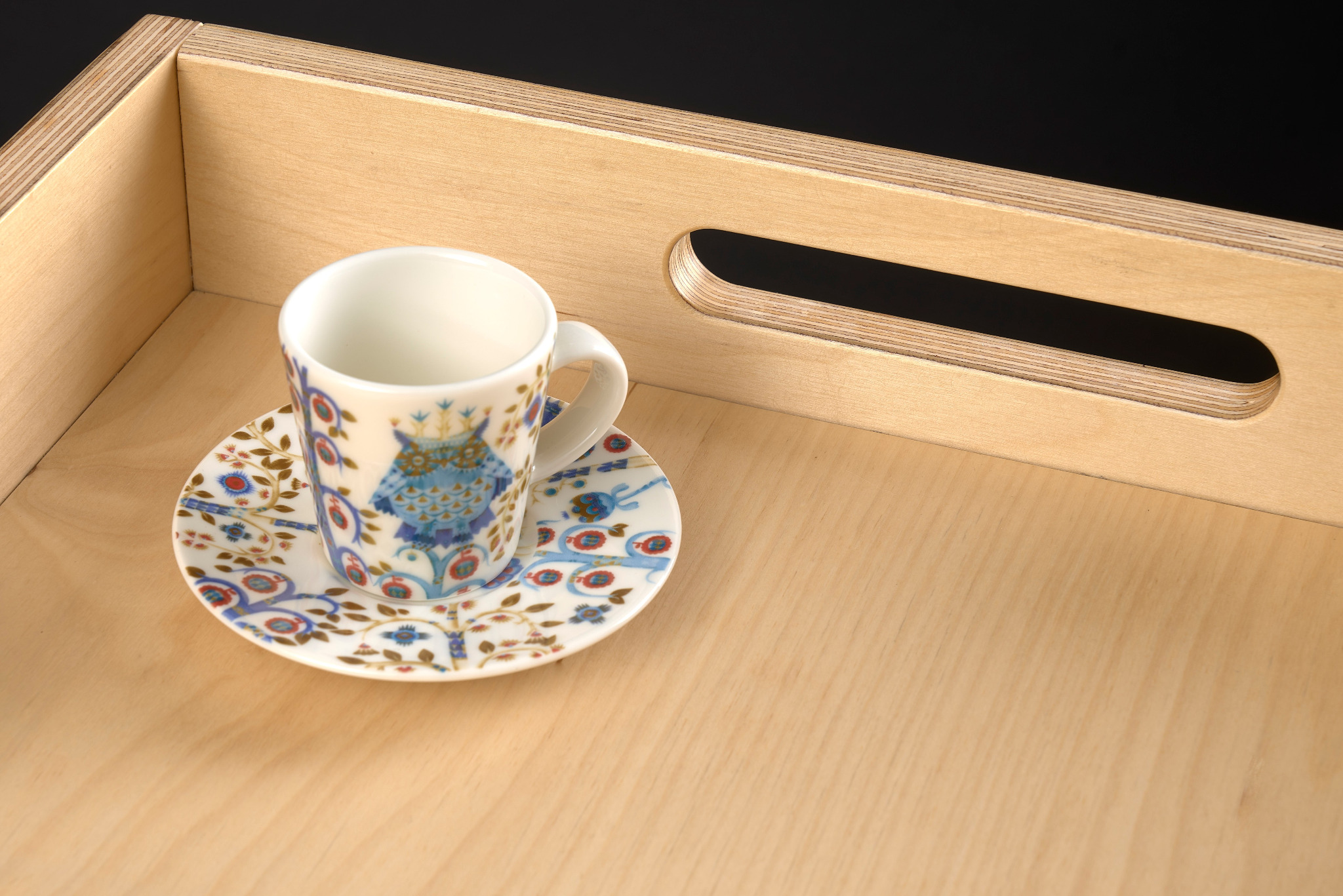 Jasna, sklejona taca z wyciętymi uchwytami, na której stoi filiżanka z podstawką w stylu retro, z motywem sowy.