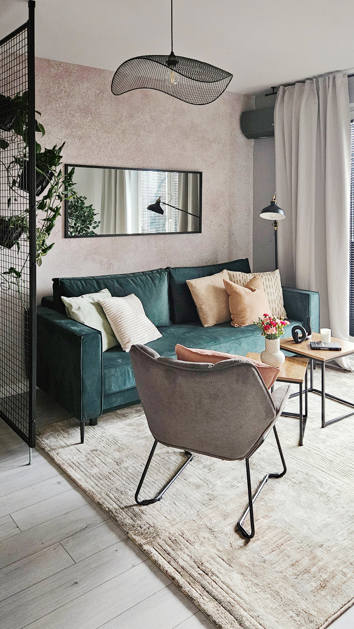 Nowoczesny salon z turkusową sofą, geometryczną lampą i metalową ścianką działową z zielenią, podkreślony jasnym dywanem i drewnianą podłogą.