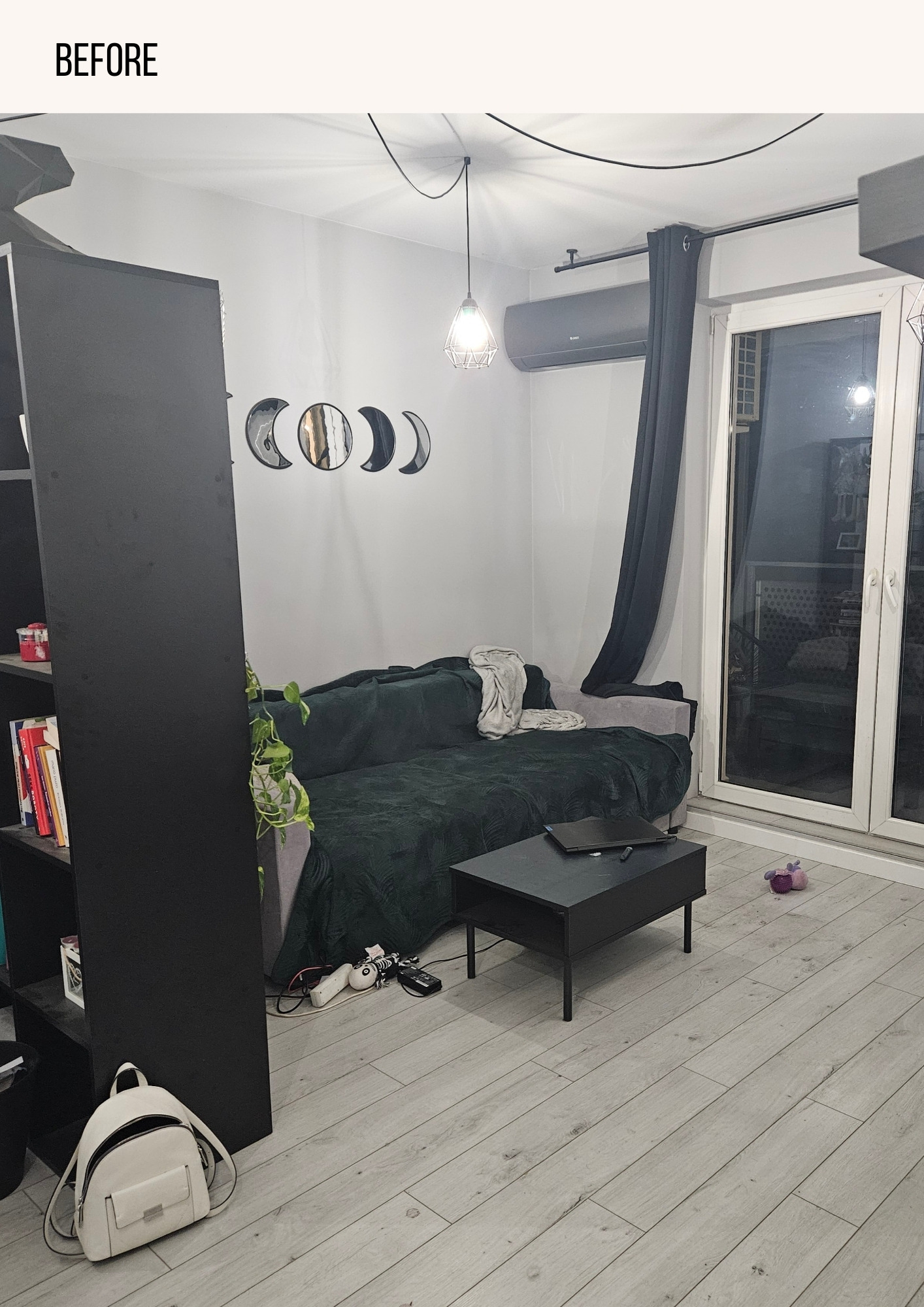 Pokój dzienny przed remontem: szara podłoga laminowana, ciemnozielona sofa z narzutą, czarny stolik kawowy z laptopem, dekoracje ścienne w kształcie faz księżyca, biały plecak na podłodze.