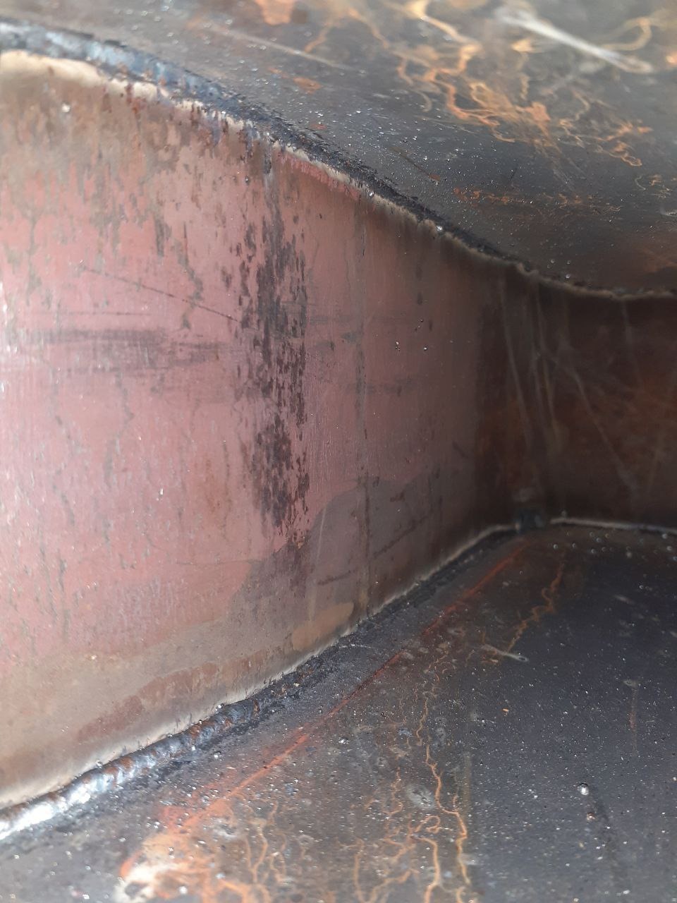 Wnętrze metalowej konstrukcji z widocznymi spawami, śladami korozji i niedoskonałościami powierzchni.