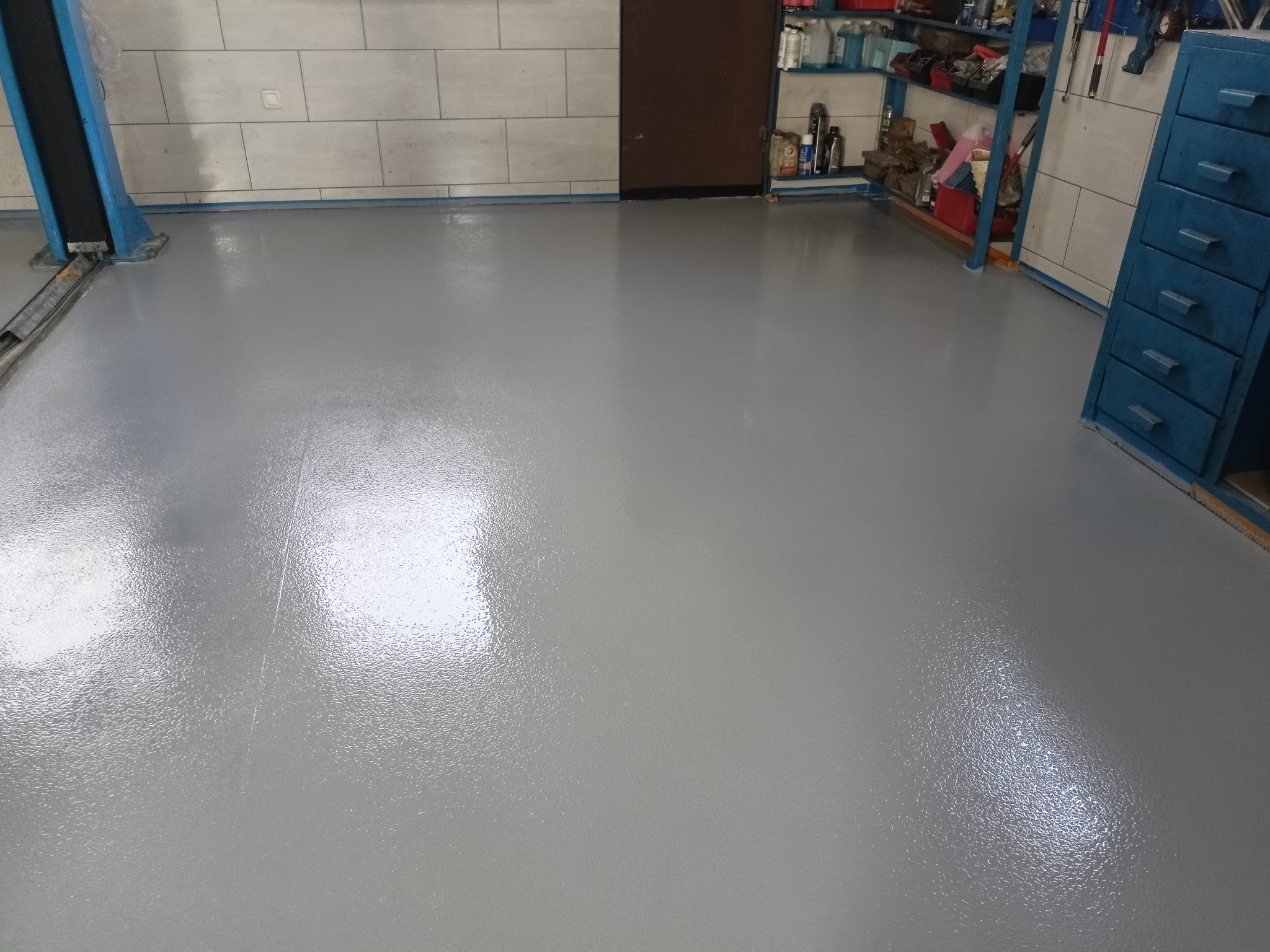 Szara, błyszcząca posadzka żywiczna w garażu, świeżo wylana, zabezpieczona taśmą malarską przy ścianach. Realizacja w Brzegu.