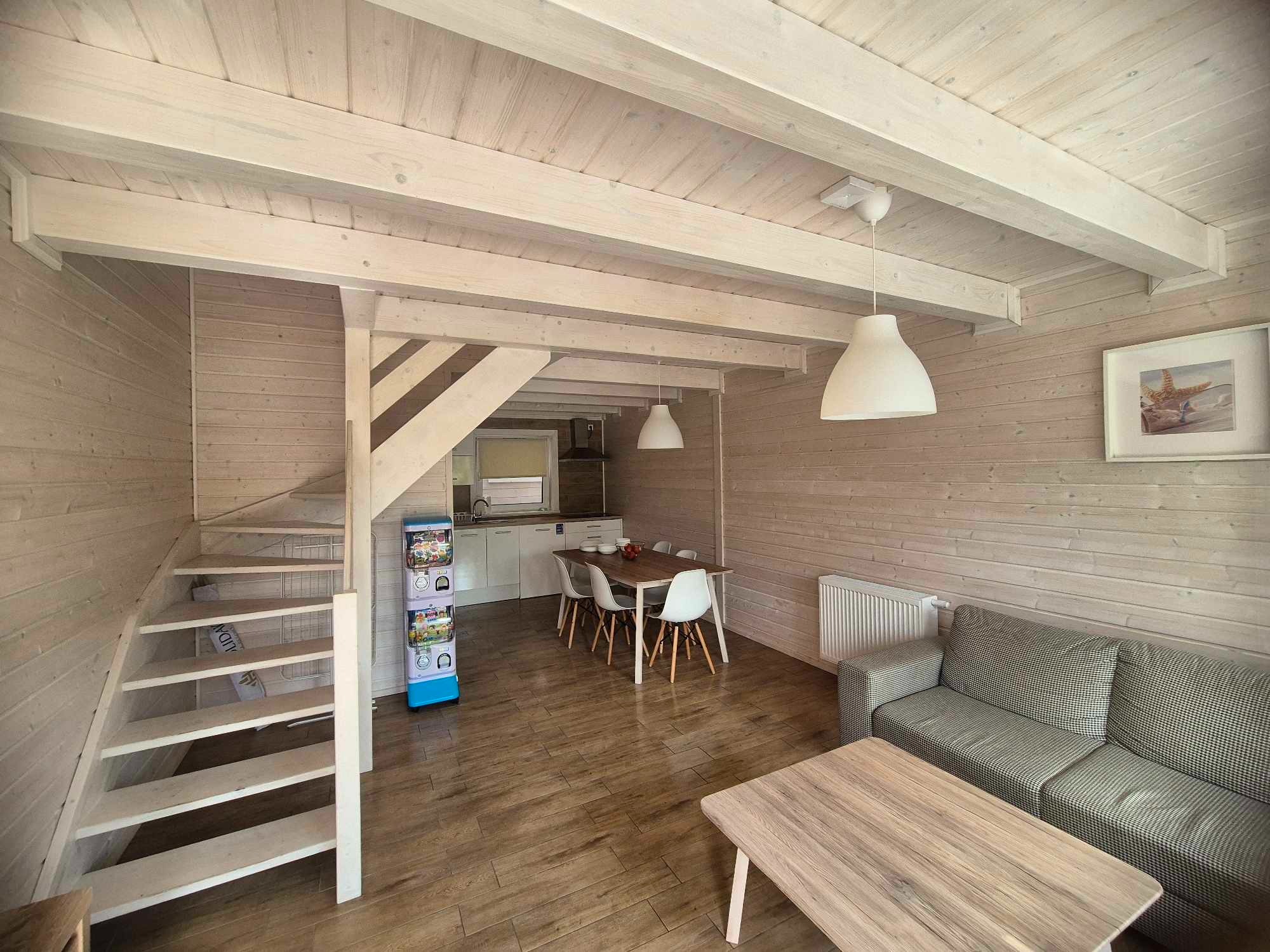 Jasne, drewniane wnętrze domu z widocznymi schodami, stołem jadalnym, sofą i elementami dekoracyjnymi, utrzymane w minimalistycznym stylu.