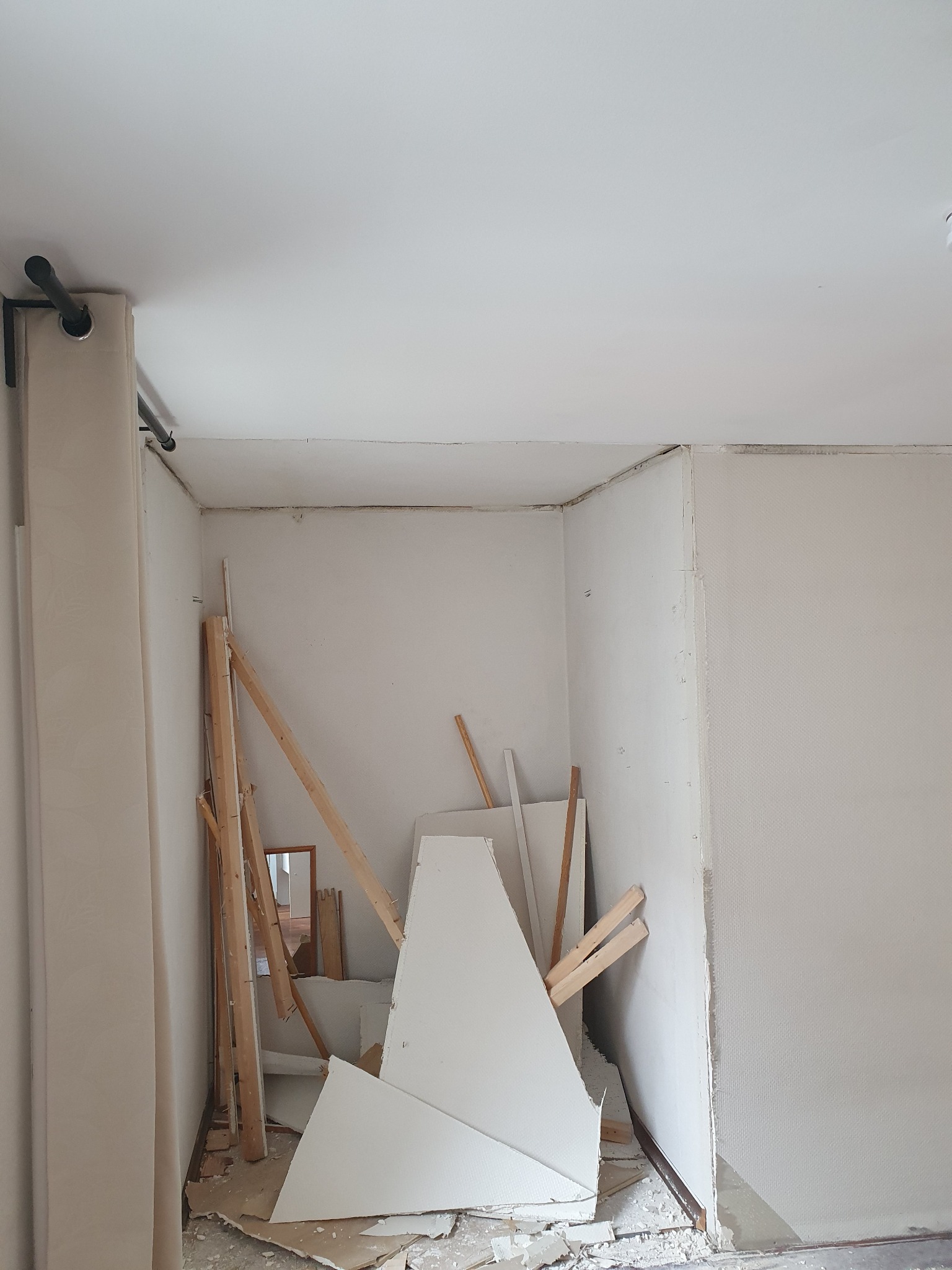 Pokój w trakcie demontażu, widoczne fragmenty płyty gipsowej, drewniane elementy konstrukcyjne, surowe ściany i sufit.