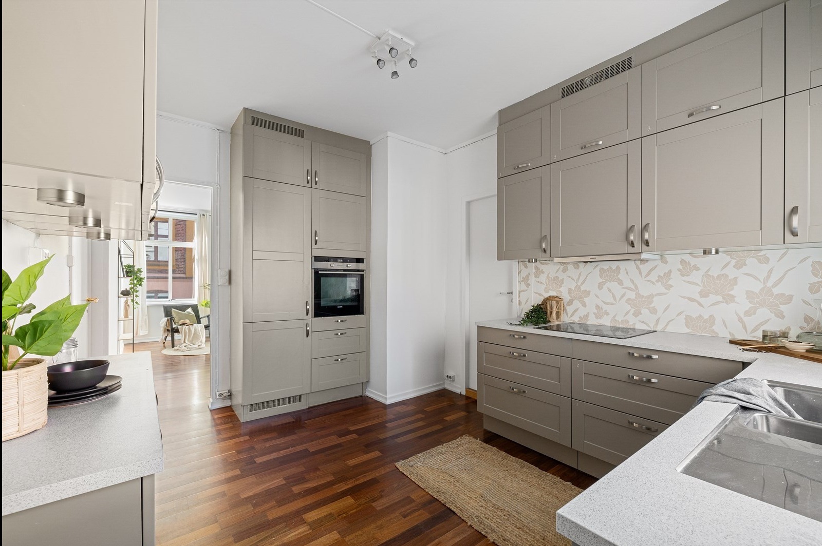 Jasnoszara kuchnia z drewnianą podłogą i wzorzystą ścianą nad blatem, widok na salon w tle.