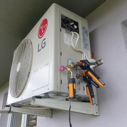Strefa AC Sławomir Smoter - Zewnętrzna jednostka klimatyzacji LG Dual Inverter zamontowana na ścianie budynku, z podłączonymi narzędziami diagnostycznymi, w trakcie serwisu.