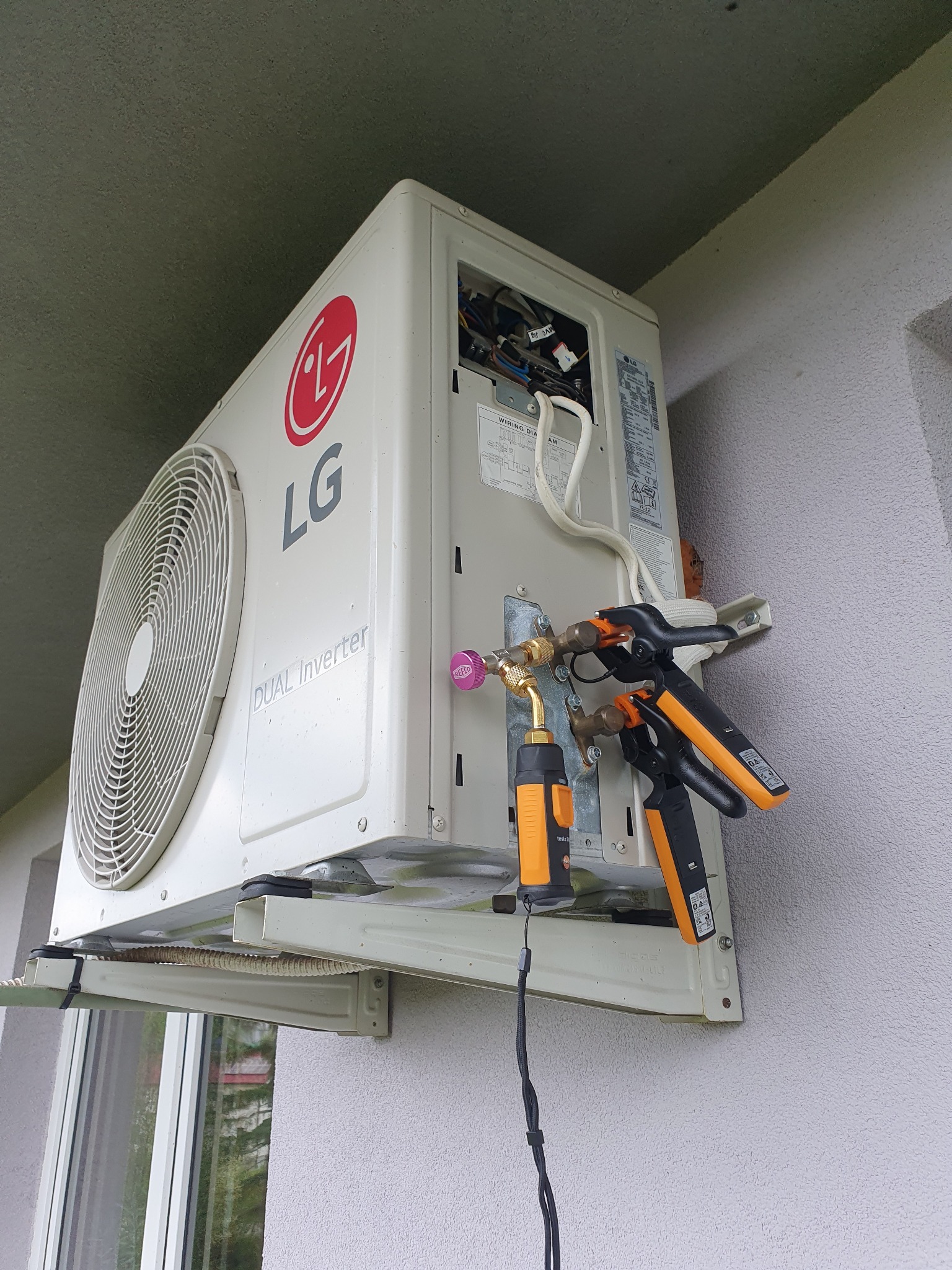 Zewnętrzna jednostka klimatyzacji LG Dual Inverter zamontowana na ścianie budynku, z podłączonymi narzędziami diagnostycznymi, w trakcie serwisu.