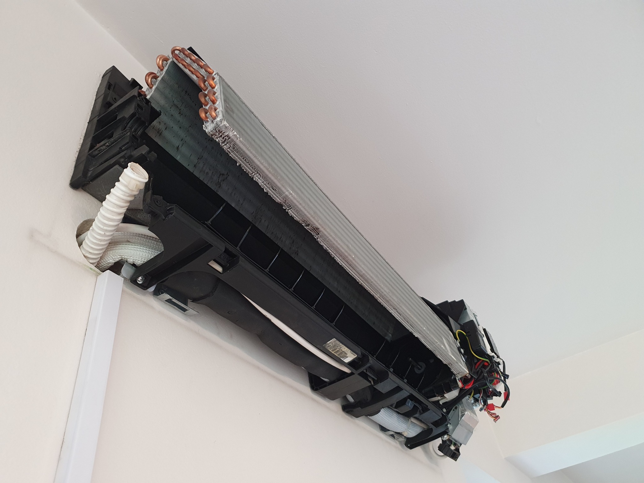 Wnętrze rozmontowanej jednostki klimatyzacyjnej na ścianie, widoczne elementy chłodzące, rurki miedziane i przewody elektryczne.