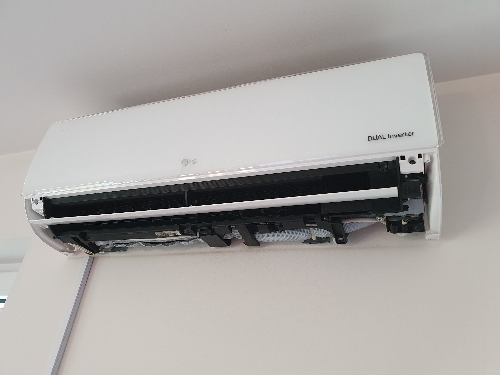 Biała jednostka wewnętrzna klimatyzacji LG Dual Inverter zamontowana na ścianie, z otwartą obudową ukazującą wewnętrzne elementy.