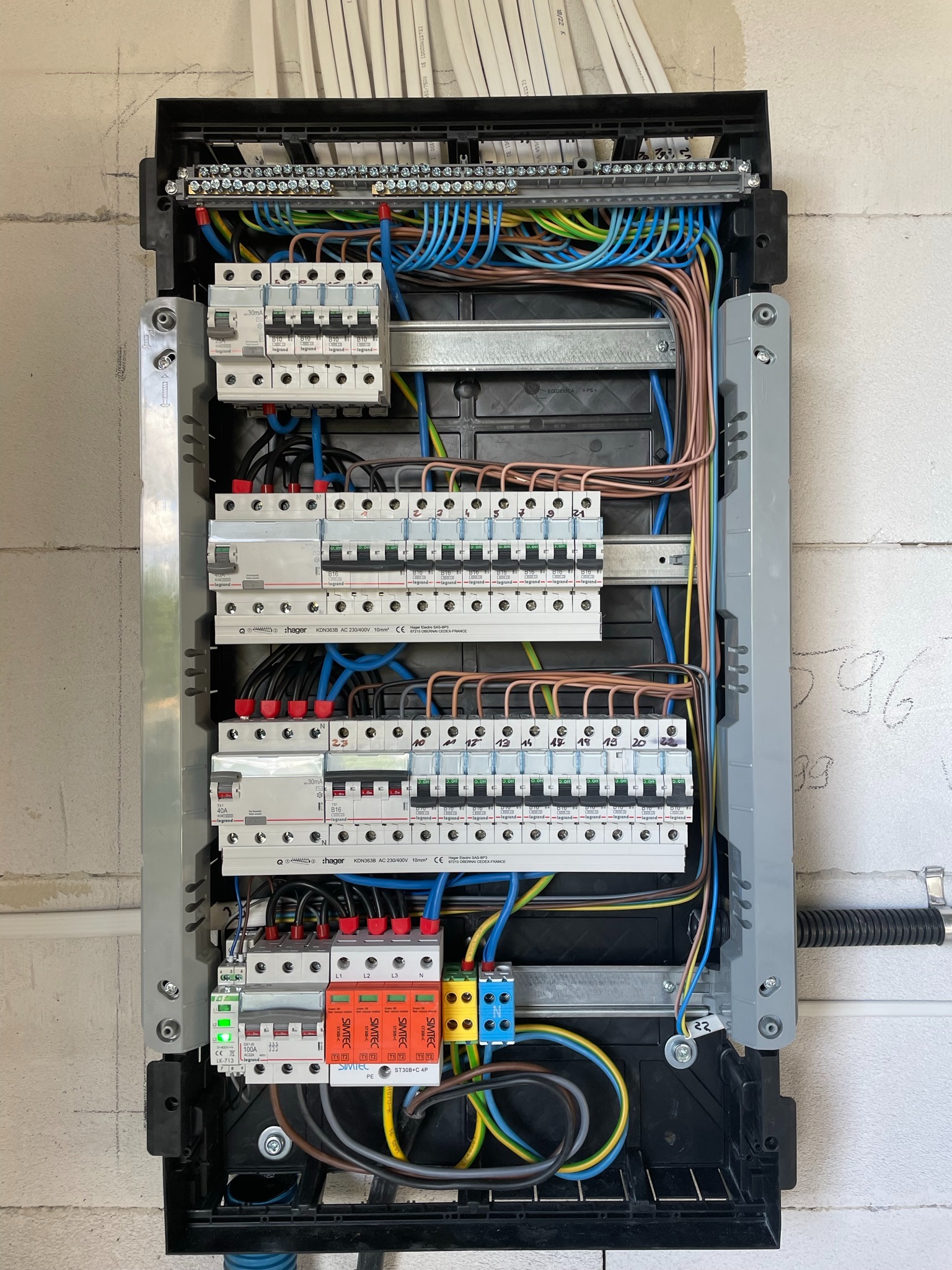 Rozdzielnica elektryczna z zainstalowanymi bezpiecznikami i przewodami różnych kolorów, zamontowana na ścianie z białych bloczków.