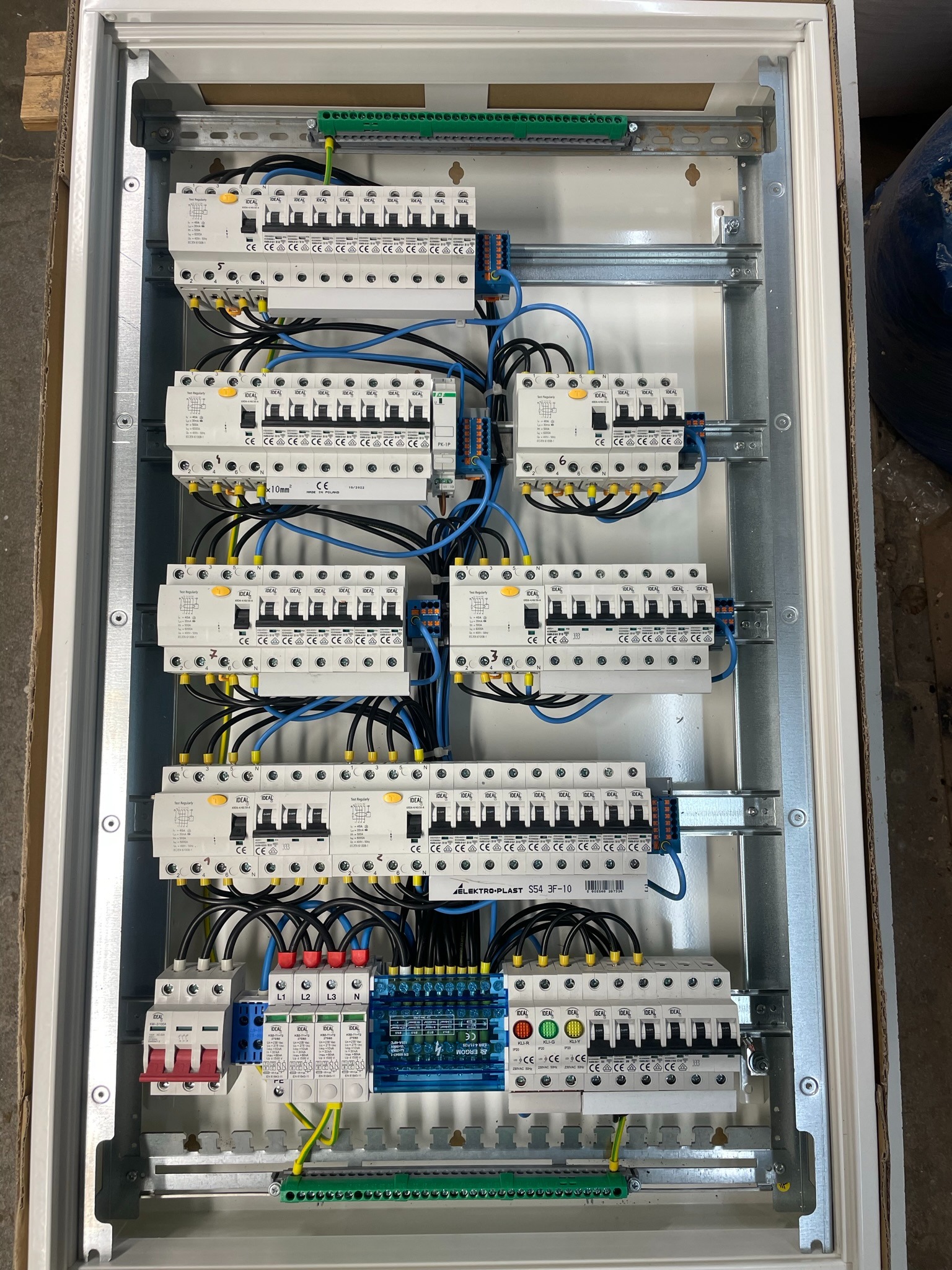 Rozdzielnica elektryczna z zamontowanymi bezpiecznikami i przewodami, widok z góry, wewnątrz metalowej obudowy.