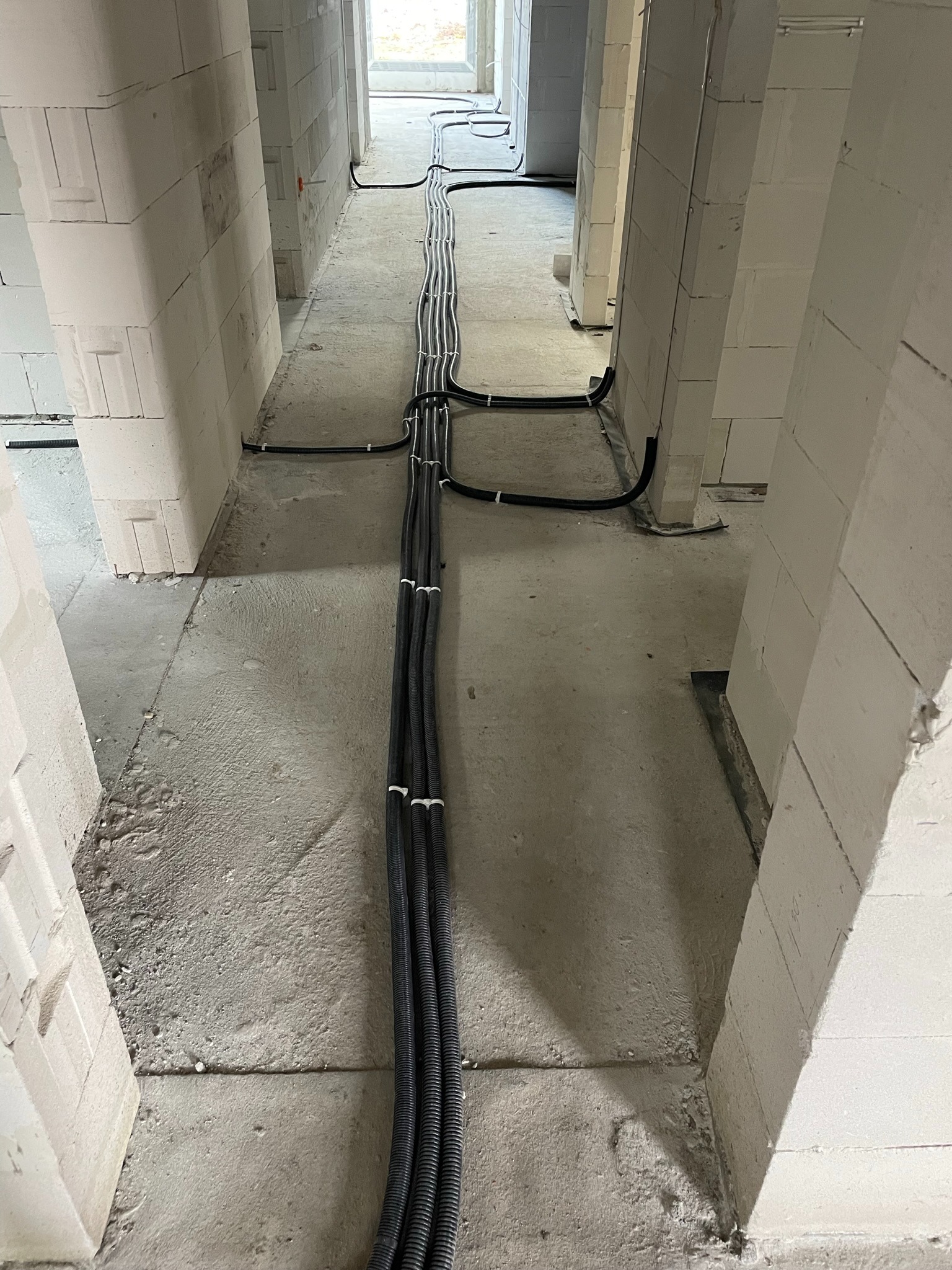 Wiązka czarnych peszli elektrycznych ułożona wzdłuż surowej ściany z betonu komórkowego w trakcie budowy domu.