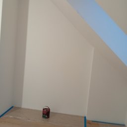 Usługi remontowo budowlane Sufity i wykończenia - Pomalowane na biało poddasze ze skosami, zabezpieczone folią i taśmą malarską. Na podłodze puszka farby i akcesoria malarskie. Widok z dołu, ukończony etap prac.