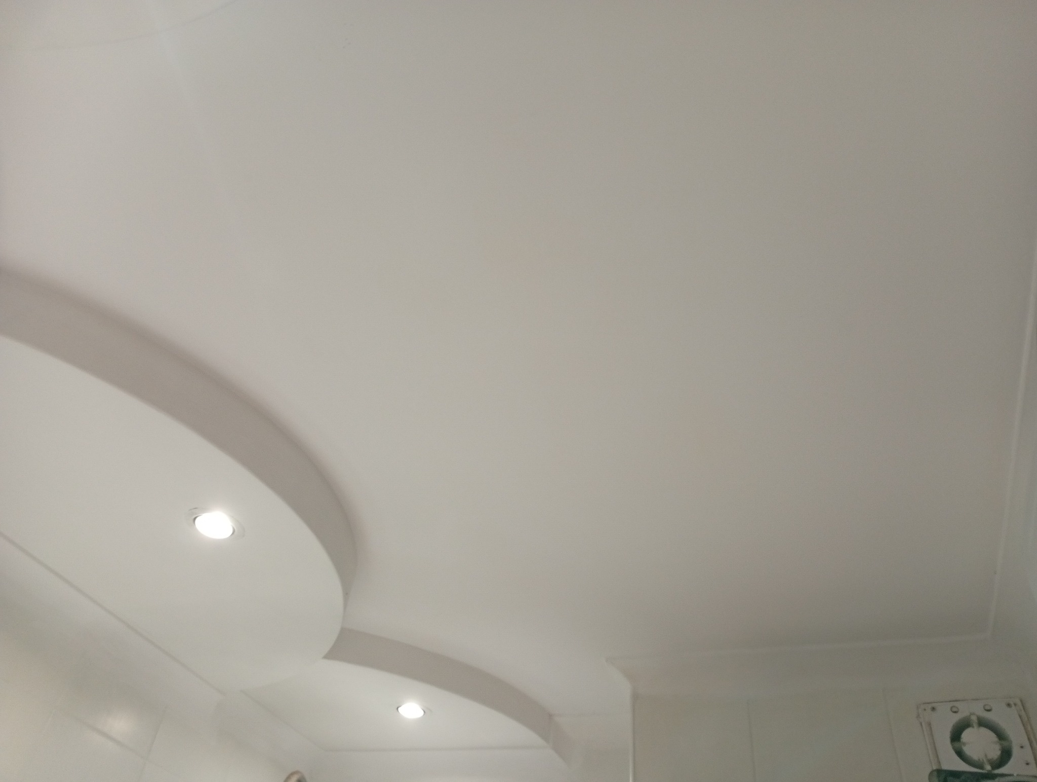 Biały sufit napinany z wbudowanymi okrągłymi lampami LED, widok z dołu, fragment wentylacji w rogu. Gładka powierzchnia sufitu.