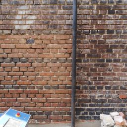 RADIUS LABS SP. Z O.O. | CZYSZCZENIE LASEREM - Mieszana ściana z czerwonej cegły z pionową rurą, fragmentem niebieskiego urządzenia z czerwonym przyciskiem i stertą cegieł u podstawy.