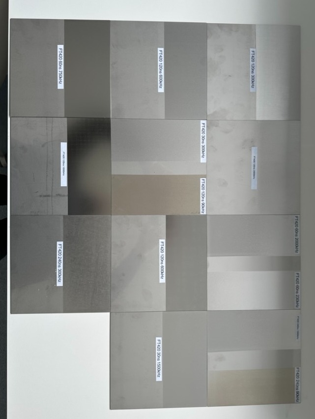 Metalowe próbki z różnymi wykończeniami powierzchni, oznaczone etykietami z parametrami obróbki, ułożone na białym tle.