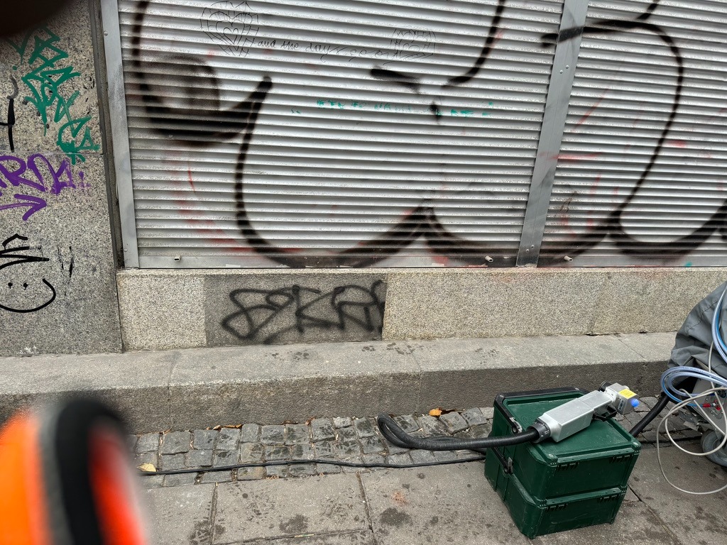 Sprzęt do usuwania graffiti ustawiony przed ścianą pokrytą graffiti i zamkniętymi żaluzjami.