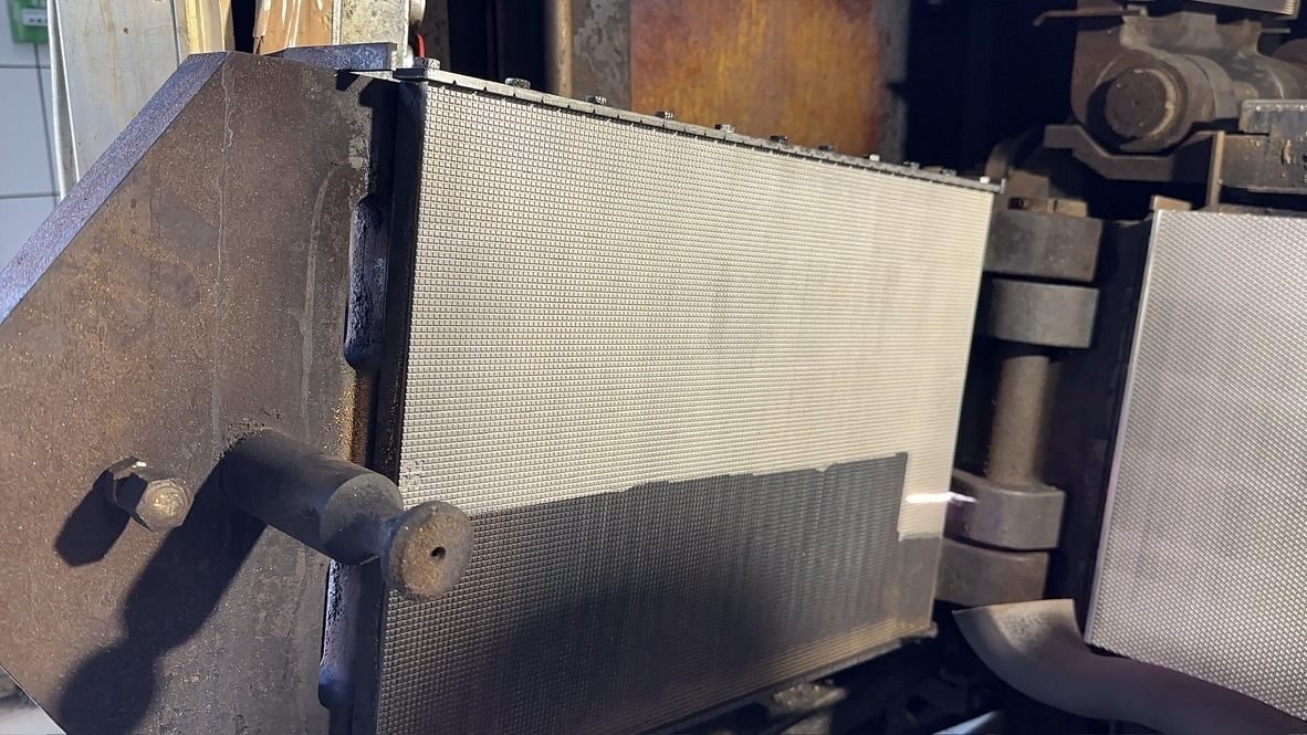 Metalowa konstrukcja z perforowanym panelem, prawdopodobnie element większej maszyny przemysłowej, z widocznymi śladami użytkowania i rdzawymi nalotami.