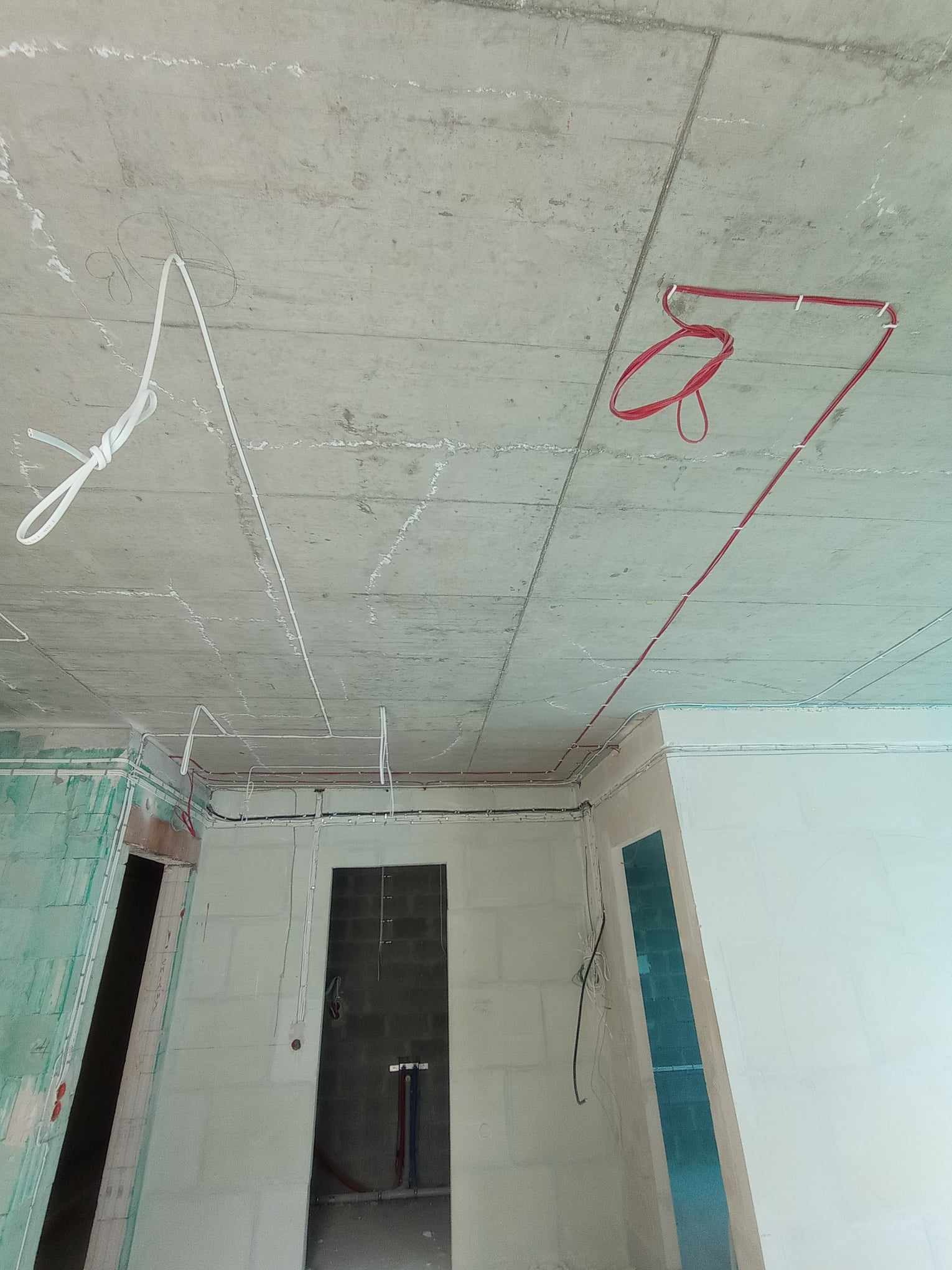 Surowy betonowy sufit i ściany w trakcie remontu z poprowadzonymi przewodami elektrycznymi w kolorze białym i czerwonym, przytwierdzonymi uchwytami, widok z dołu w pomieszczeniu z widocznymi...