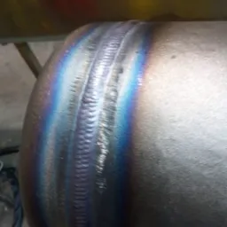 Spoina na metalowej rurze, widoczne tęczowe przebarwienia termiczne.