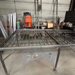 Krzysztof Sołtys - Wykonywanie konstrukcji metalowej kraty na stole spawalniczym w warsztacie, widoczna spawarka Kemppi, butla z gazem i narzędzia.