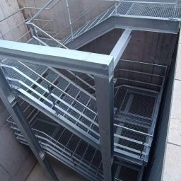 Krzysztof Sołtys - Metalowe schody z kratką w betonowym szybie, widok z góry, oświetlenie naturalne.