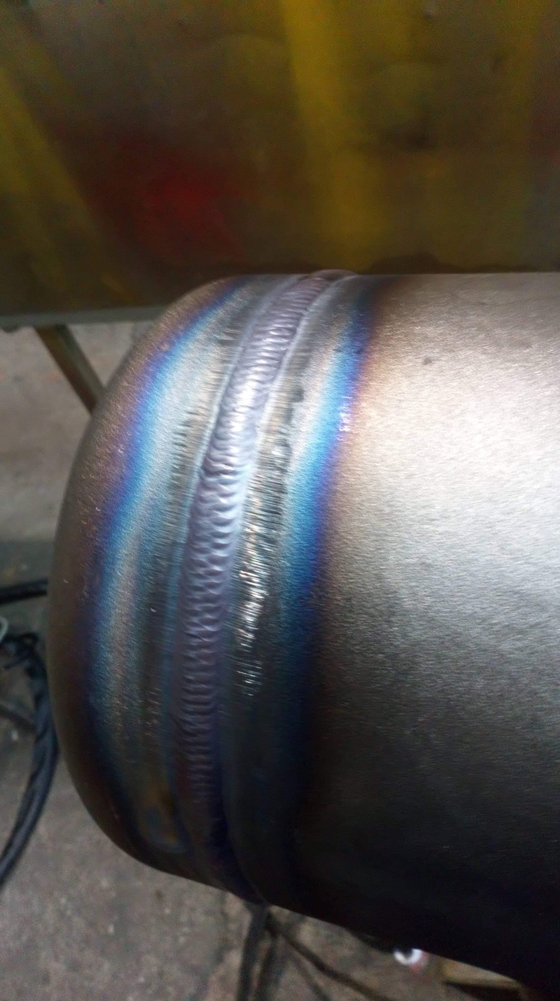 Spoina na metalowej rurze, widoczne tęczowe przebarwienia termiczne.