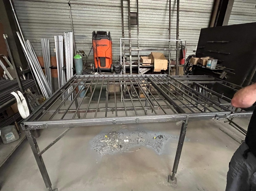 Wykonywanie konstrukcji metalowej kraty na stole spawalniczym w warsztacie, widoczna spawarka Kemppi, butla z gazem i narzędzia.