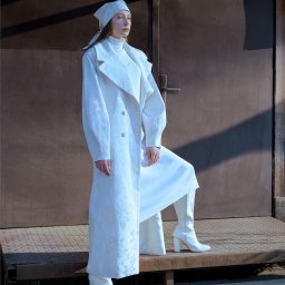 Paulina Wyszyńska-Górecka Photography & Marketing - Kobieta w białym, wzorzystym płaszczu i kozakach na tle metalowych drzwi z cieniem.