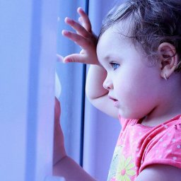 Paulina Wyszyńska-Górecka Photography & Marketing - Dziewczynka z niebieskimi oczami, w różowej koszulce w kropki, opiera dłoń o szybę okna, patrząc na zewnątrz.