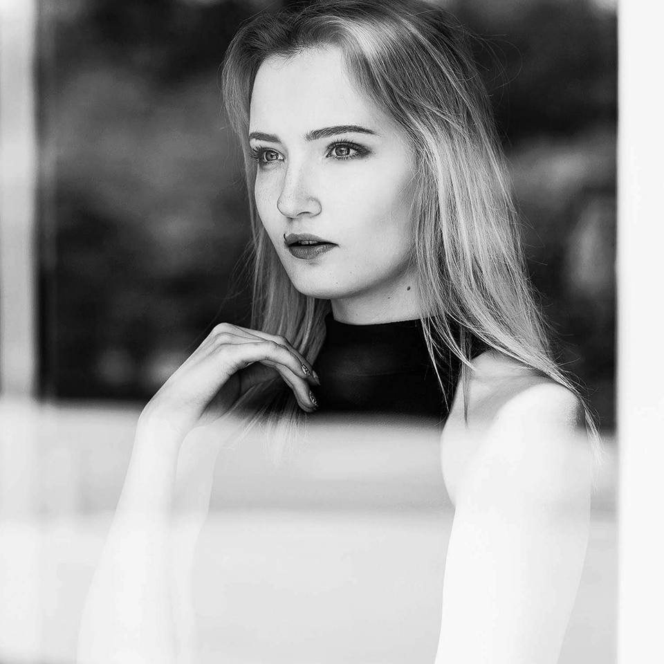 Portret kobiety z długimi blond włosami, czarno-białe zdjęcie, skupiony wzrok, delikatny makijaż, pozuje przy oknie.