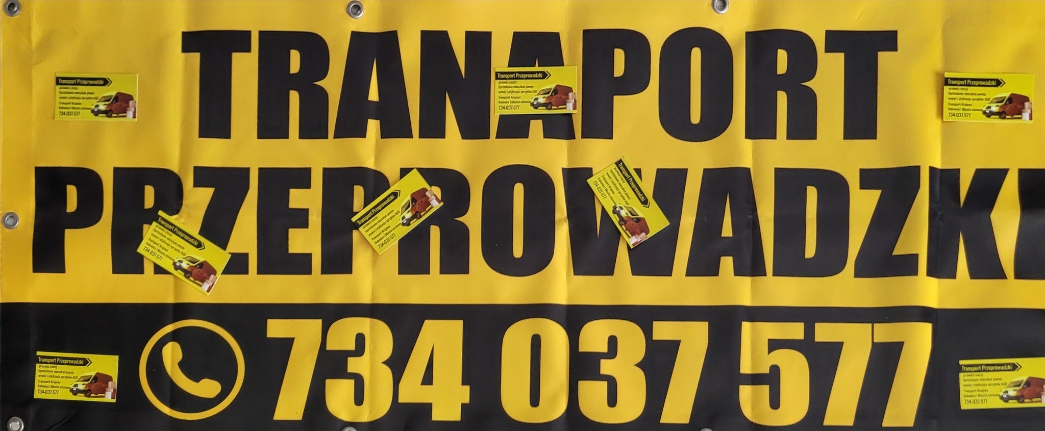 Żółto-czarny baner reklamowy z napisem 'TRANSPORT PRZEPROWADZKI' i numerem telefonu, ozdobiony wizytówkami firmy oferującej przewóz rzeczy.