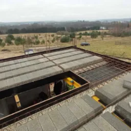 Budowa stropu Teriva: betonowe pustaki ułożone na konstrukcji zbrojeniowej, widoczne ż&oacute;łte paczki Ytong, krajobraz w tle.