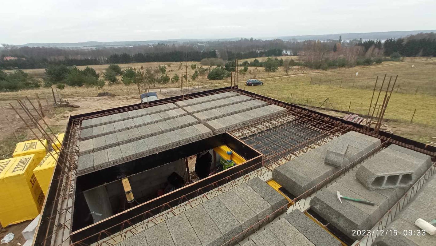 Budowa stropu Teriva: betonowe pustaki ułożone na konstrukcji zbrojeniowej, widoczne żółte paczki Ytong, krajobraz w tle.