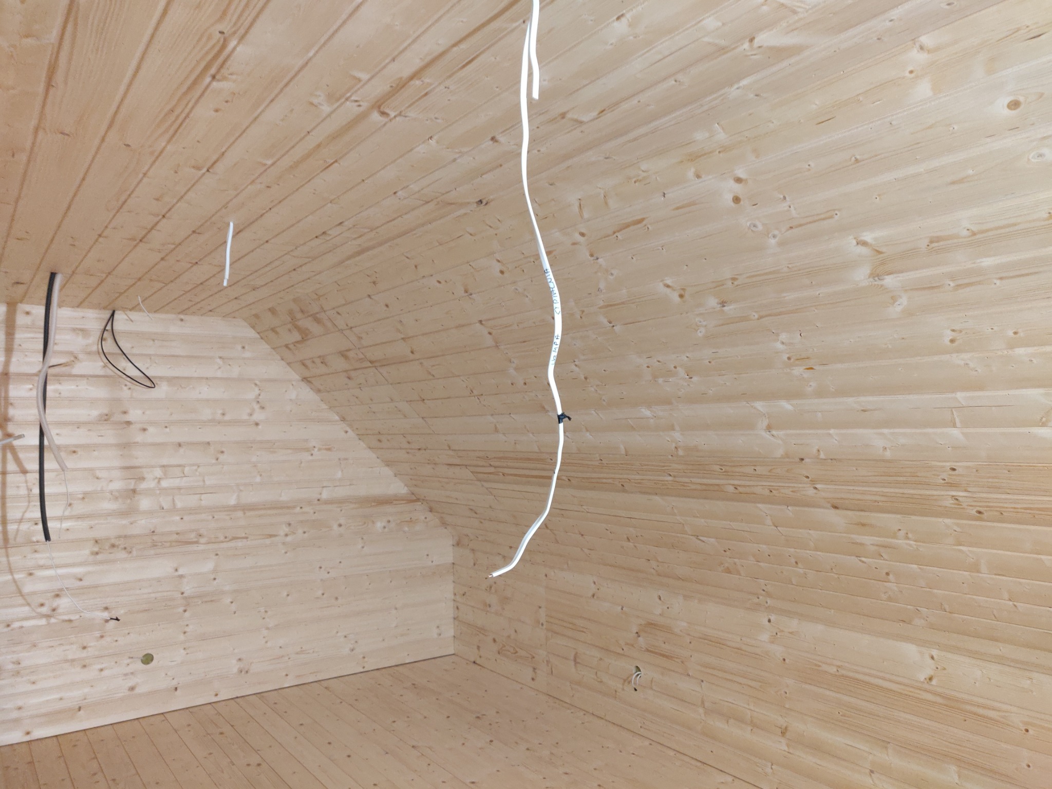 Wnętrze domu szkieletowego z widoczną drewnianą konstrukcją ścian, poddasza i podłogi oraz wystającymi przewodami elektrycznymi.