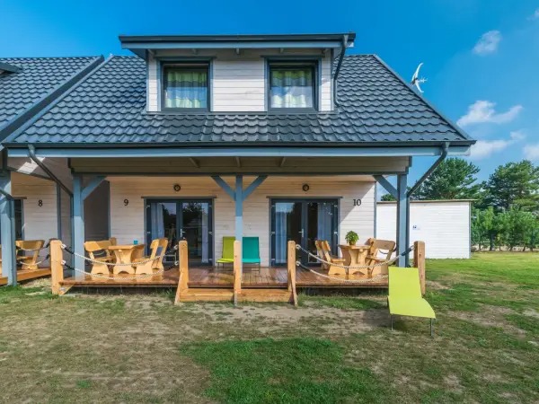 Domy szkieletowe z ciemnoszarą dachówką i drewnianym tarasem z meblami ogrodowymi, numery budynków 9 i 10.