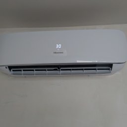 MS Sanit Michał Słobodzian - Biały klimatyzator Hisense zamontowany na ścianie z widocznymi śladami po malowaniu i niebieską taśmą malarską przy krawędzi ściany.