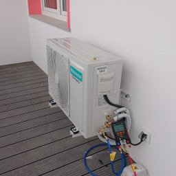 MS Sanit Michał Słobodzian - Biała jednostka zewnętrzna klimatyzacji Hisense zamontowana na wspornikach na tarasie z desek kompozytowych, podłączona do miernika ciśnienia z przewodami, obok narzędzia.